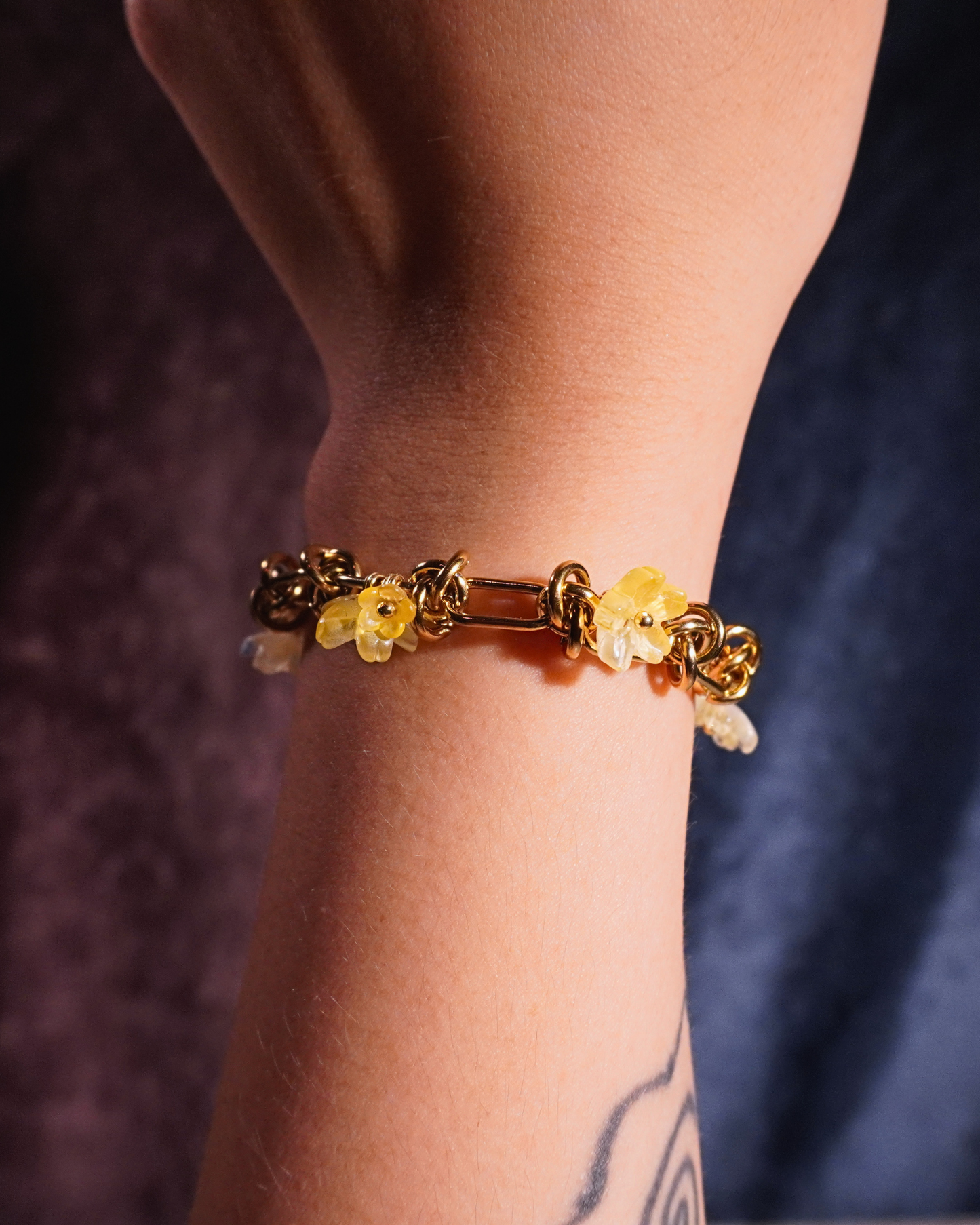 Gold bracelet with yellow beads on a wrist against a dark background