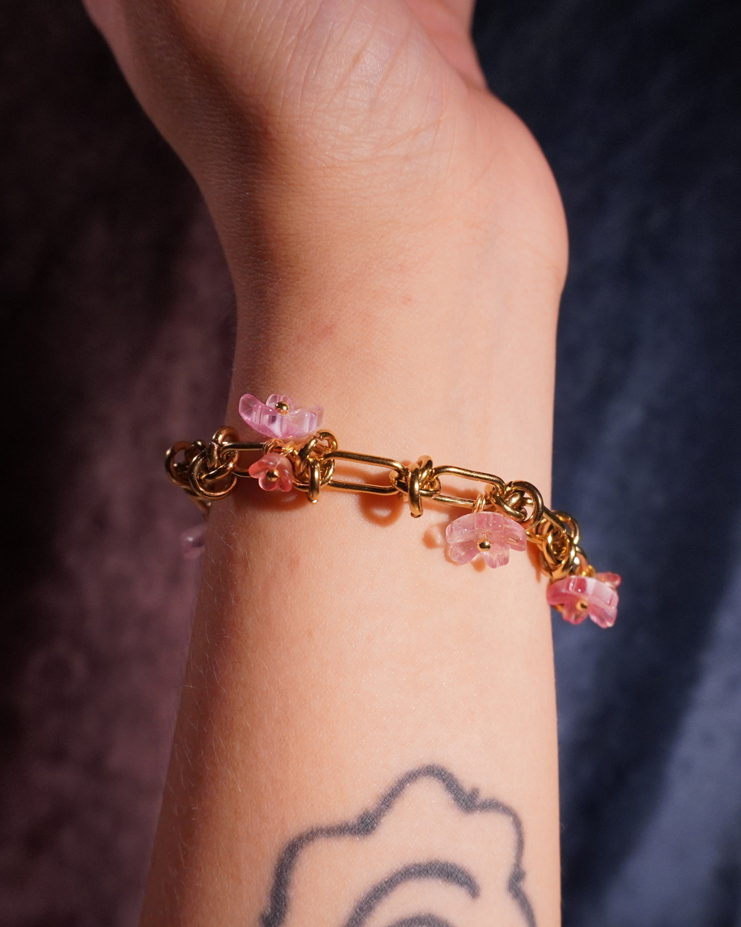 Bracelet with pink floral charms on a wrist against a dark background