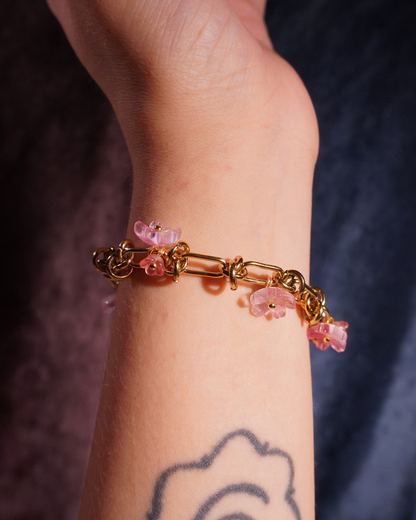 Bracelet with pink floral charms on a wrist against a dark background