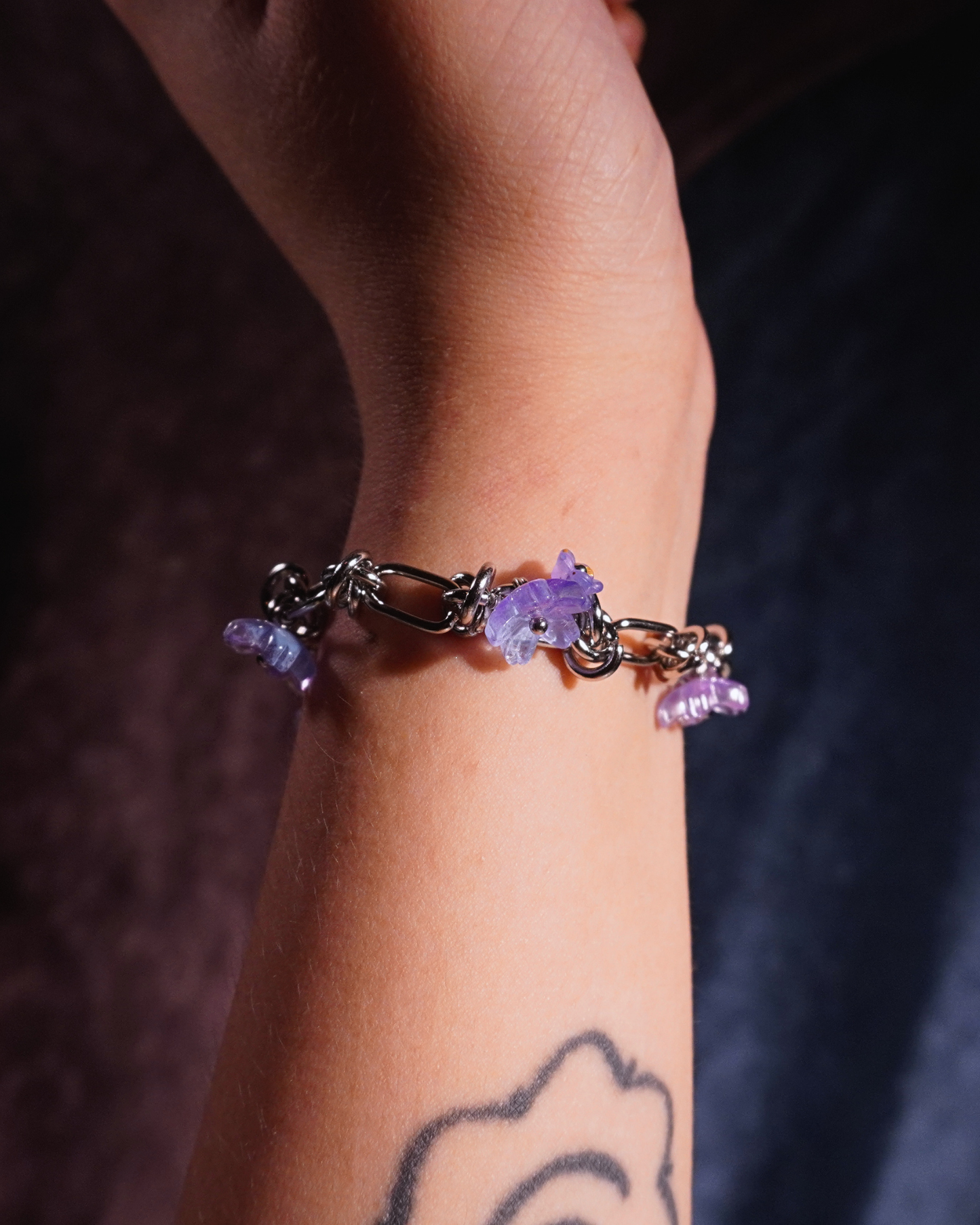 Silver bracelet with purple flowers on a wrist against a dark background