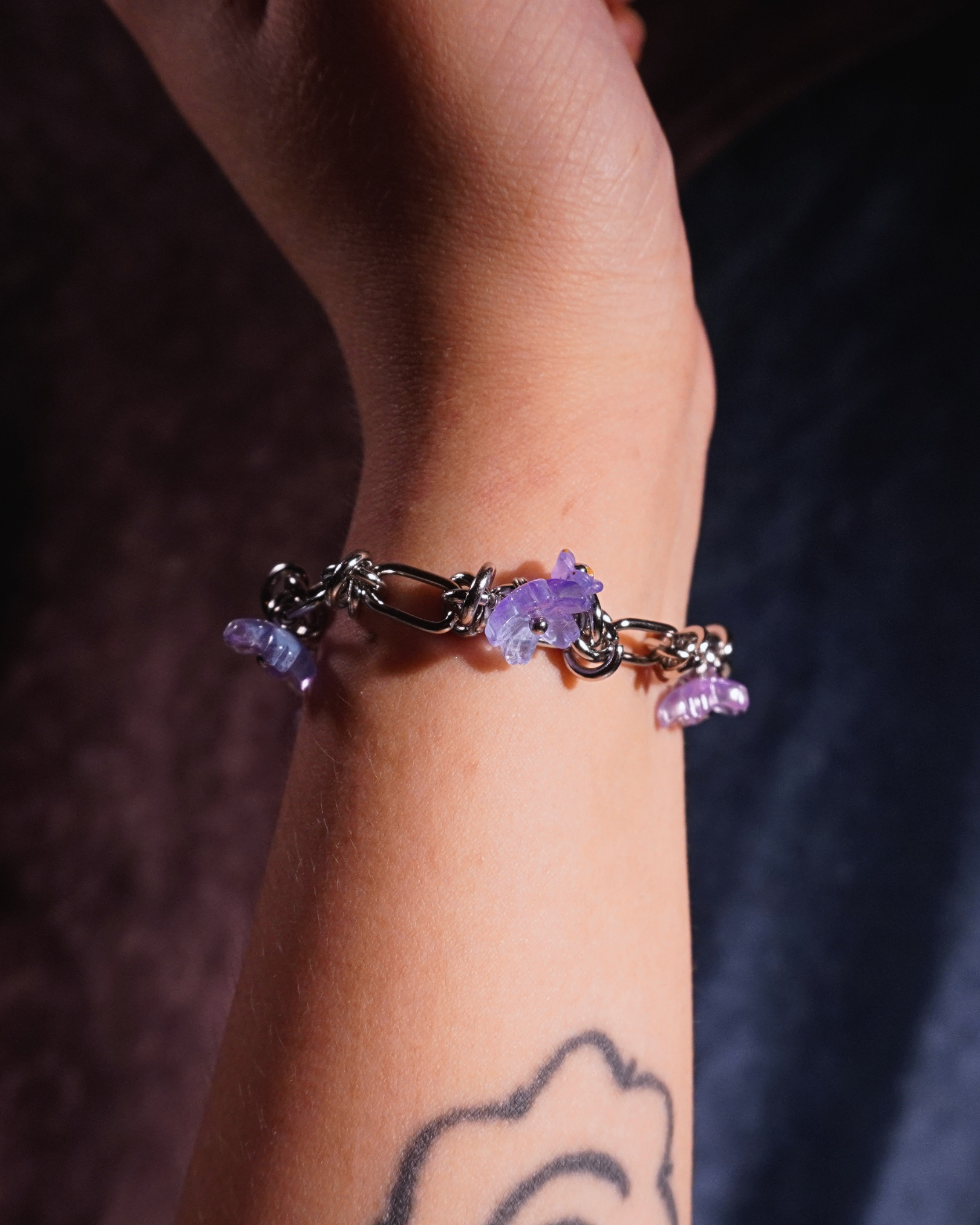 Silver bracelet with purple flowers on a wrist against a dark background
