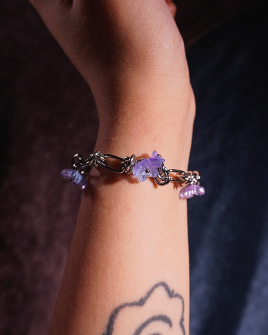 Silver bracelet with purple flowers on a wrist against a dark background
